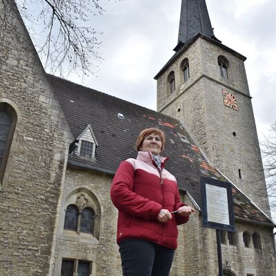 Gemeindekirchenrats-Vorsitzende Burga Kinzel vor der Nordseite der Gröninger Martini-Kirche. Am Turm sind jüngst Schäden über der Glockenstube beseitigt worden.